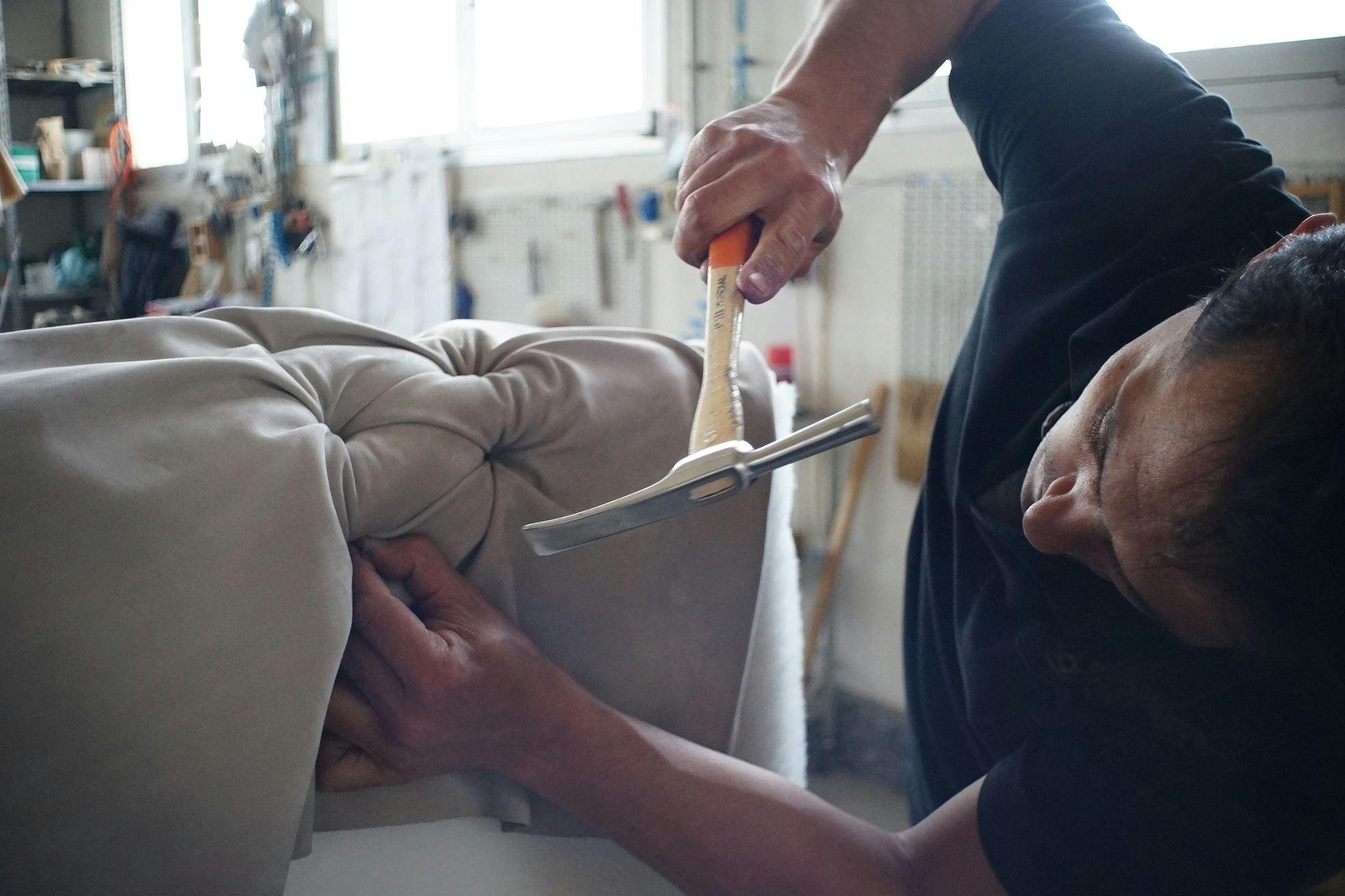 Skilled artisan working meticulously on a sofa using upholstery tools in a workshop.